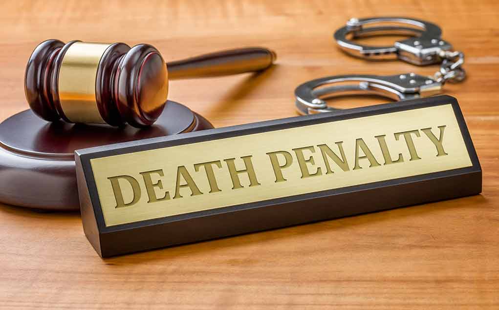 Gavel, handcuffs, and a nameplate reading death penalty on a wooden desk