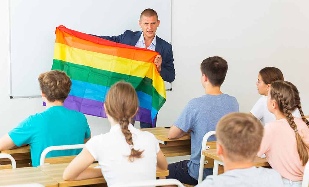 Teacher holding a rainbow pride flag in front of students