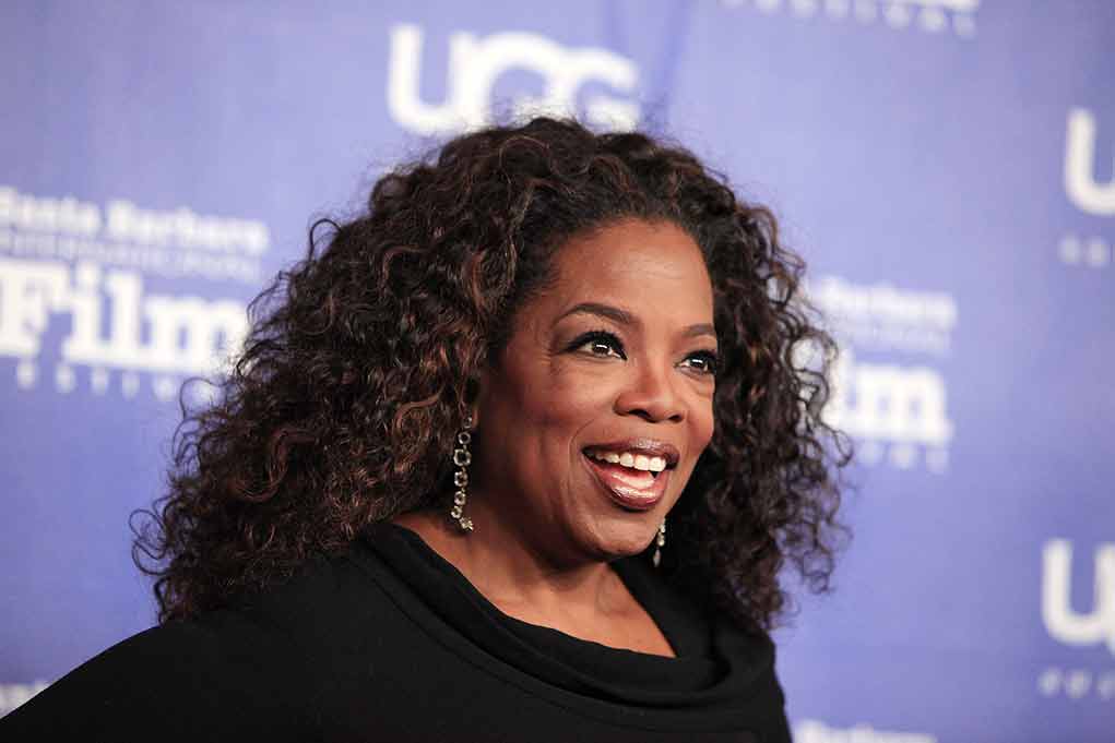 smiling woman with curly hair on a blue step-and-repeat backdrop