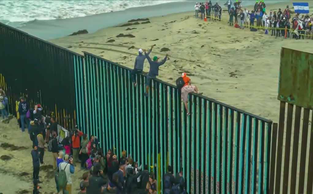 People climbing a tall beachside border fence