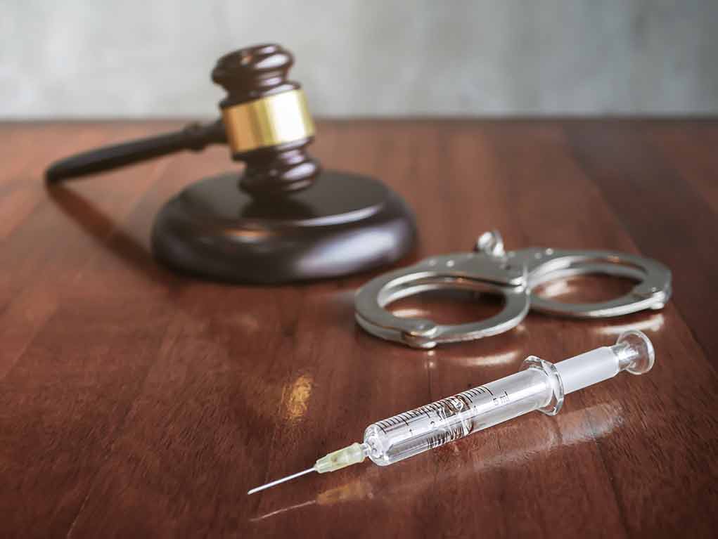 Syringe beside handcuffs and a judge's gavel on a wooden table