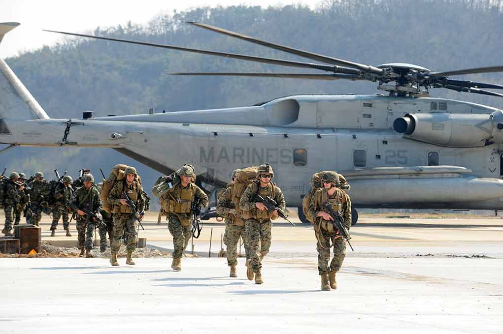 Soldiers disembark and walk past a large military helicopter